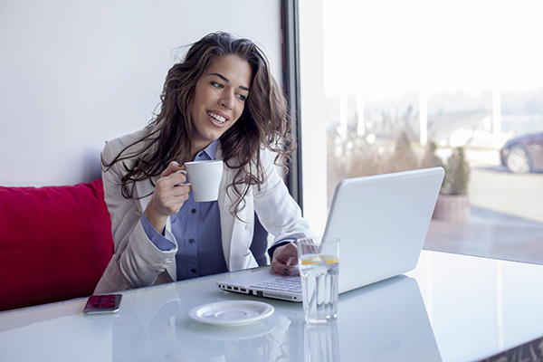 Mujer sentada tomando cafe y mirando a su computadora